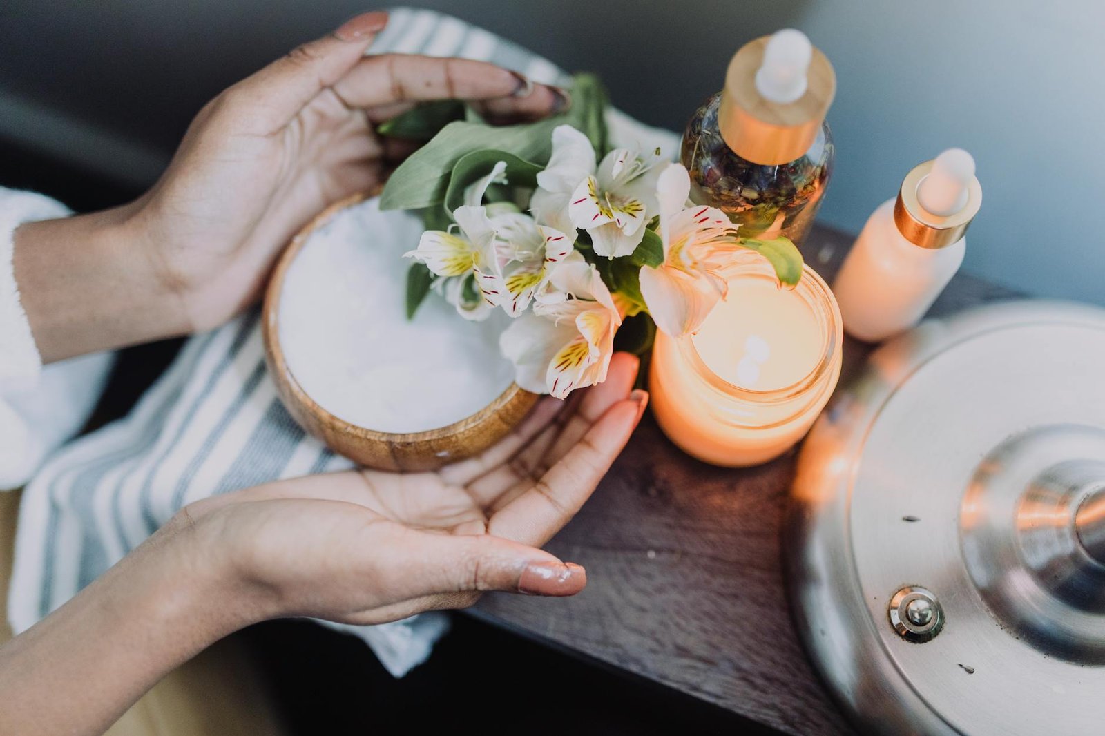 A calming spa scene featuring hands holding flowers beside candles and skincare products.