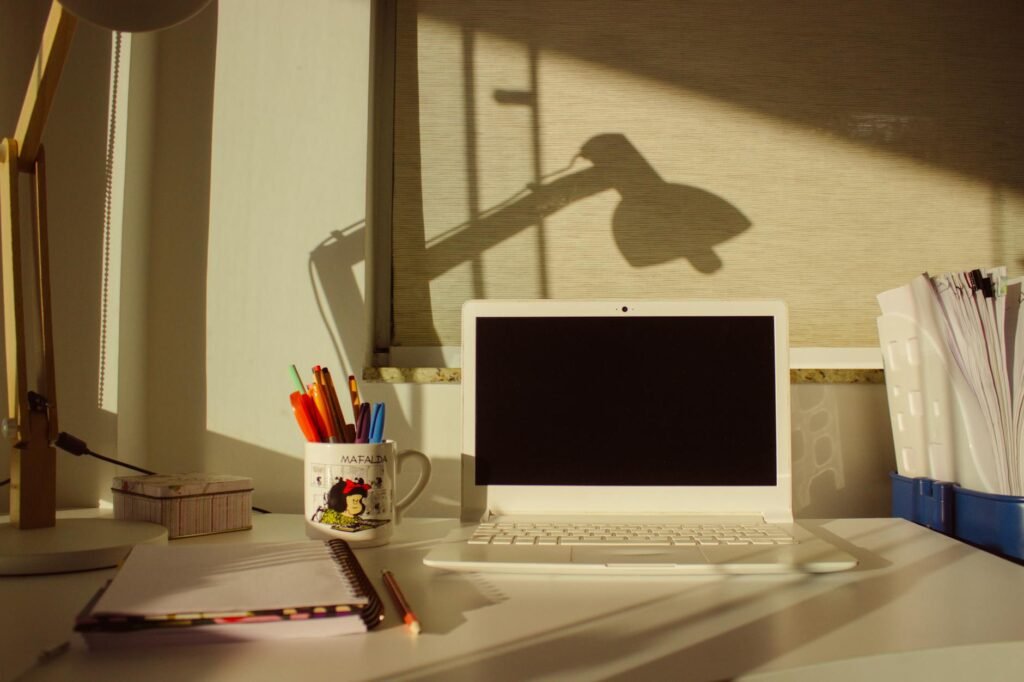 A well-organized home office desk with a laptop, stationery, and warm lighting.