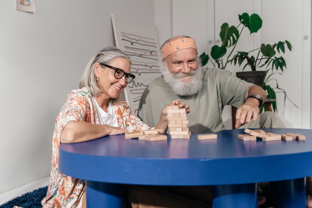 Elderly couple playing Jenga indoors, enjoying leisure time together at a blue table.
